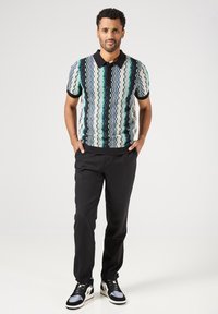 Pánská polokošile s krátkým rukávem a pleteným vzorem v zelené, modré a krémové barvě. Kombinována s černými, ušitými kalhotami a sportovními černými a modrými teniskami.