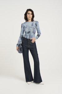 Maglietta azzurra a maniche lunghe, con texture e dettagli arricciati, abbinata a pantaloni flare in denim scuro. La modella tiene una clutch grigia. Scarpe bianche a punta.