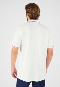 Camiseta polo blanca con un diseño clásico, que presenta ribetes rojos en el cuello y las mangas, confeccionada en tejido suave y con un corte relajado.