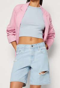 Ljusblå denimshorts med slitna detaljer, tillsammans med en figurnära ljusblå crop top och en välarbetad rosa blazer.
