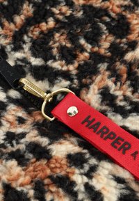 Zwarte rits op een multicolore wolstof met een rode stoftrekker gelabeld "HARPER & YVE" en een gouden metalen ritslider.