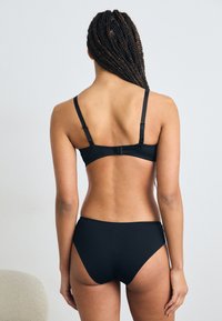 Svart bikinisets med en enkel design, justerbara remmar och en krokspänne på baksidan. Tygerna verkar släta och elastiska.