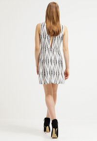 Mekko, jossa on mustavalkoinen kuvio, V-muotoinen selkä, olkaimettomat hihat ja liehuva hame. Mallilla on mustat nilkkurit.