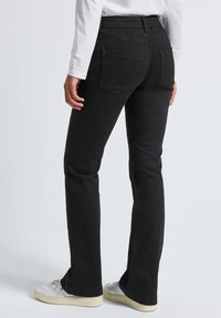 Jean flare en denim noir avec taille mi-haute, dotés de poches arrière et d'une texture lisse ; stylés avec des baskets blanches.