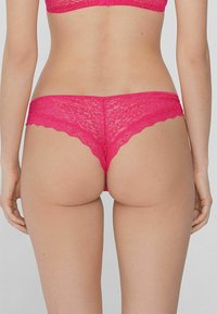Roze kanten string met golvende randen, voorzien van intricates bloempatronen en een gladde textuur. De achterzijde toont een ontwerp met minimale bedekking.