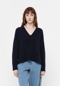 Maglione a maglia blu navy con scollo a V, texture a coste sull'orlo e sui polsini, caratterizzato da una vestibilità rilassata. Abbinato a jeans di denim azzurro.