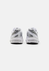 Hvite athletic sneakers med sølvfargede detaljer, mesh-paneler og teksturerte gummis�åler; har polstret krage og reflekterende elementer.