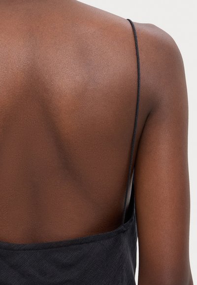 Black spaghetti strap dress with a low back design; smooth texture and a fitted silhouette, showcasing a minimalist and elegant style.