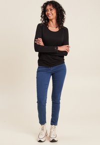 Schwarzes Langarmoberteil mit Spitze an den Schultern und Manschetten, kombiniert mit blauen Skinny-Jeans und weißen Sneakers. Lockere Passform, glatte Textur.