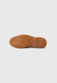 Semelle en caoutchouc marron d'une chaussure, présentant une surface texturée avec des motifs circulaires et des stries horizontales, design plat avec une épaisseur modérée.