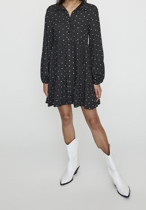 Černé bavlněné šaty s bílými puntíky, zapínání na knoflíky vpředu, límeček, dlouhé rukávy a vrstvená sukně. Kombinované s vysokými bílými špičatými kovbojskými botami.