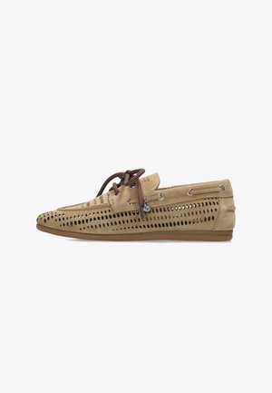 Zapato náutico de ante beige con diseño perforado, cordones marrones y detalles de ojales metálicos. Suela plana de goma. Construcción simple y transpirable.
