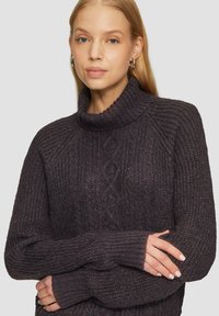 Dunkelgrauer, gestrickter Pullover mit hohem Kragen, geripptem Textil und Rautenmuster. Die langen Ärmel haben gerippte Bündchen für zusätzlichen Komfort.