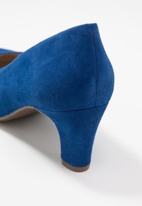 Chaussure à talon haut en daim bleu avec un bout arrondi et un talon modéré. Texture lisse avec des coutures soignées et un design ouvert à l'avant.