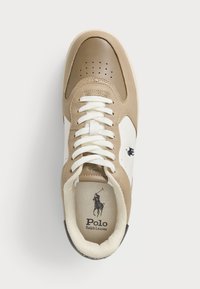 Baskets Polo Ralph Lauren beiges et blanches avec lacets blancs, bout perforé et logo du joueur de polo noir sur le côté et sur la semelle intérieure.