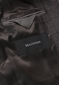 Forro interior negro con una textura suave, que presenta un bolsillo gris y una etiqueta cosida con "Matinique" en letras blancas.