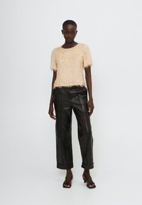 Top corto a maniche corte di un beige chiaro e morbido abbinato a pantaloni in pelle nera a vita alta con taglio dritto e risvolti.