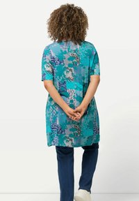Tunic blu e teal con motivo, a maniche corte, vestibilità ampia, che arriva a metà coscia, abbinata a jeans di denim scuro e sneakers chiare.
