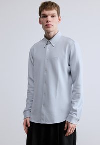 Svetlosivá košeľa s dlhým rukávom s textúrovaným povrchom, golierom na gombíky, prednými gombíkmi a malým logom vyšitým na ľavej strane hrudníka.