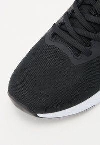 Fekete sportcipő hálós felsőrésszel, textúrált felülettel és fűzőkkel. Gumiból készült orrész és mintázott tapadós fehér talp jellemzi.