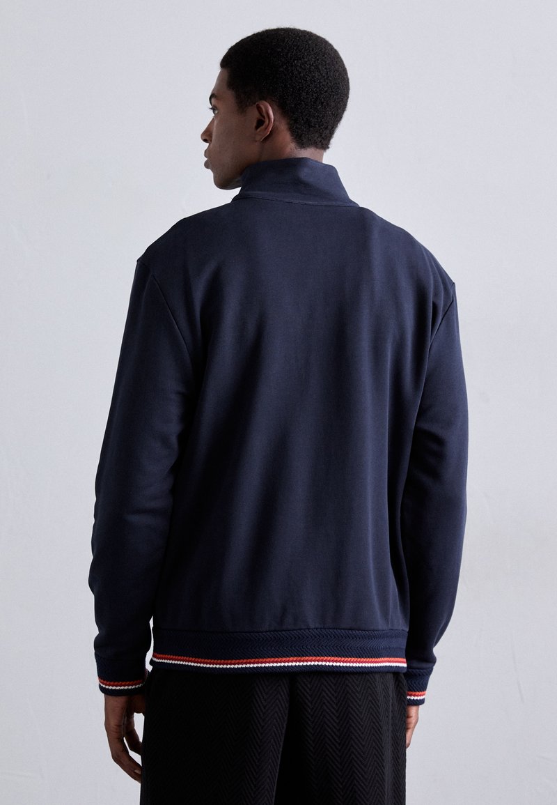 Navyblaues Sweatshirt mit hohem Kragen, gerippten Bündchen und einem farbigen gestreiften Akzent am Saum. Hergestellt aus einem glatten, weichen Stoff.