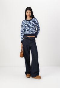 Blue knit sweater with heart pattern and ribbed cuffs, paired with dark denim wide-leg pants, and brown platform shoes. Brown handbag included.