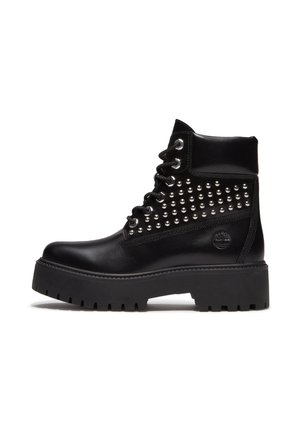 Bottine noire en cuir à lacets avec clous argentés, semelle épaisse à crampons, col rembourré et logo de marque embossé sur le côté du talon.