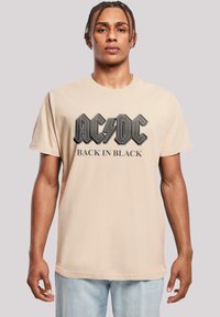Beige cotton t-shirt featuring AC/DC logo in black with lightning bolt; short sleeves and crew neck design.