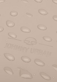 Világos bézs textúrájú felület kiemelkedő cseppekkel; tartalmazza a "JOHNNY URBAN" logót és minimalista dizájnt.