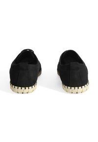 Chaussures en daim noir avec une surface texturée, présentant une semelle tissée blanc cassé et des coutures contrastantes le long du bord.