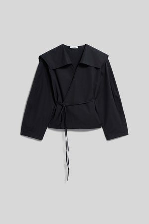 Blouse noire à manches longues, col large et détail de nouage sur le côté, posée à plat sur un fond gris clair.