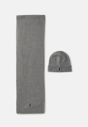 Γκρί πλεκτό κασκόλ και καπέλο στην ίδια απόχρωση, και τα δύο με ραμμένο σχέδιο. Το κασκόλ είναι μακρύ, ενώ το καπέλο έχει διπλωμένο περιθώριο και accent με λογότυπο.