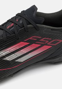 Sort sportsko med tekstureret overdel, markante røde og sølvstriber, slank design og sorte snørrebånd. Fleksibel sål for godt greb.