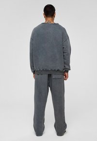 Grijze oversized sweatshirt en bijpassende broek gemaakt van zacht, textuurmateriaal. De sweatshirt heeft een versleten halslijn en elastische manchetten.