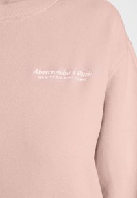 Jasnoróżowy sweatshirt wykonany z miękkiej bawełny. Posiada okrągły dekolt oraz wyszywane logo marki w białym kolorze na klatce piersiowej. Teksturowane wykończenie.