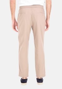 Pantaloni beige con una vestibilità comoda, due tasche posteriori e una texture liscia. Abbinati a scarpe blu navy, il tessuto ha una leggera lucentezza.