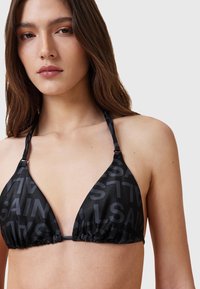 Top bikini a triangolo nero realizzato in tessuto morbido con un sottile motivo tono su tono, legacci regolabili al collo e alla schiena, lati arricciati.