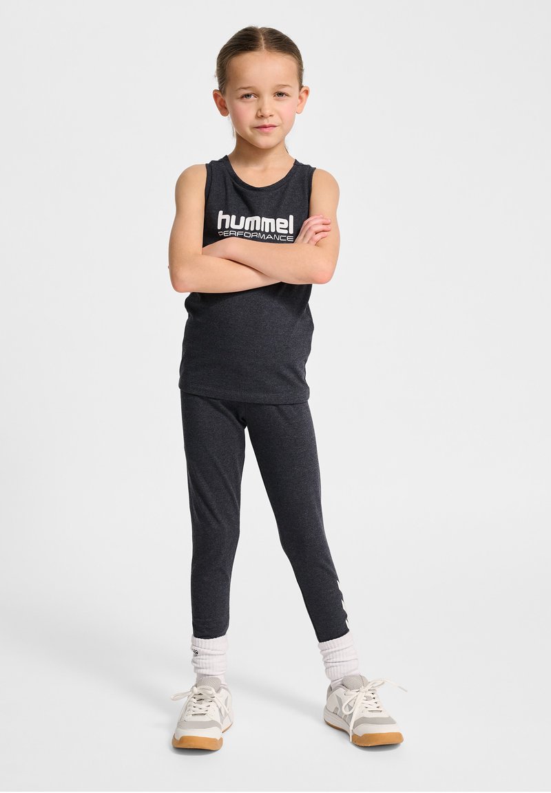 Svart ärmlös träningslinne med "hummel PERFORMANCE"-logotyp, kombinerat med svarta, åtsittande leggings. Bärs med vita strumpor och ljusa sneakers.