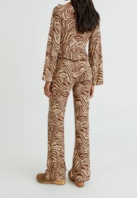 Femme portant un haut à manches longues zèbre brun et beige et un pantalon flare assorti, associé à des chaussures à plateforme brunes, se tenant de dos.