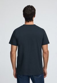 Mörkgrå bomullst-shirt med rund hals och korta ärmar, med en enkel design och slät textur, sedd från baksidan.