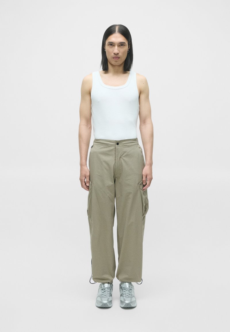 Lyseblå tanktop, beige cargo-bukser med lommer og lysegrå sneakers. Outfittet har en afslappet pasform og et enkelt design.