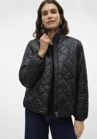 Giacca nera trapuntata con colletto alto, chiusura con zip e polsini elastici a coste. Texture liscia e motivo a rombi su tutta la superficie.