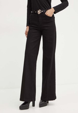 Jeans neri a gamba larga realizzati in denim, caratterizzati da una vita alta, passanti per la cintura e una cintura con logo dorato. Modello abbinato a scarpe nere con tacco largo.