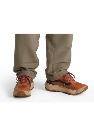 Zapatillas deportivas naranjas con acentos negros, que cuentan con una suela texturizada, un acolchado grueso y cordones a juego. Llevadas con pantalones beige claros.