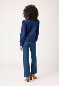 Pull en maille bleu marine avec manches bouffantes, associé à un jean bleu taille haute et des chaussures à talons carrés marron. Texture douce, coupe ajustée.