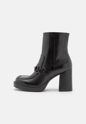 Black leather ankle boot with a rounded toe, buckle accent, and a high block heel, featuring a smooth, shiny texture and outlined stitching.