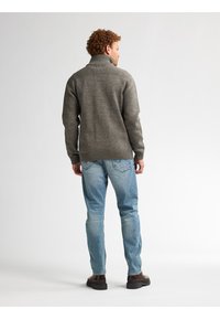 Grauer Strickpullover mit hohem Kragen und gerippten Details, kombiniert mit hellblauen Jeans und braunen Stiefeln, von hinten gezeigt.
