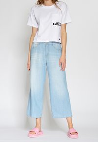 Vit kortärmad t-shirt med framficka, ljusblå vida denimjeans och rosa plattformssandaler med tjock sula.