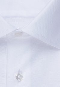 Camicia bianca in primo piano con tessuto texturizzato, dettagli con bottoni e design del colletto classico.