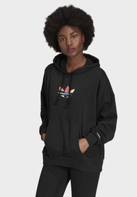 Felpa nera con tasca frontale, dotata del logo trefoil Adidas multicolore. Realizzata in tessuto morbido, ha un cappuccio con cordino e maniche lunghe.